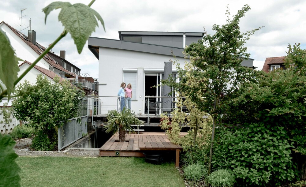 Modernes Loftgebäude mit Terrasse und Garten, zwei Personen stehen auf der Terrasse, Umbau sichtbar