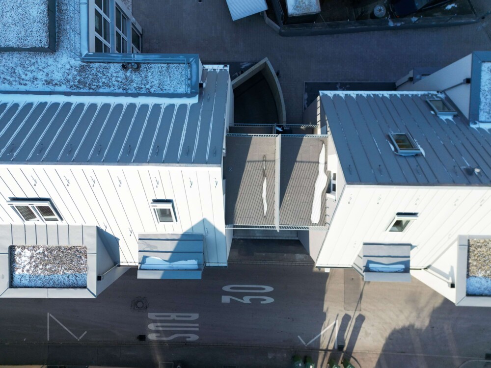 Dach eines Gebäudes mit leichtem Schneebelag, umgeben von Straßen und weiteren Häusern in einer Stadt