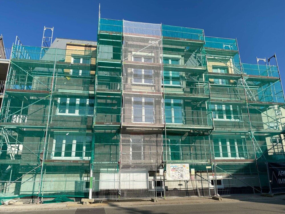 Mehrstöckiges Wohngebäude mit Gerüst und grünem Schutznetz während Fassadenbau