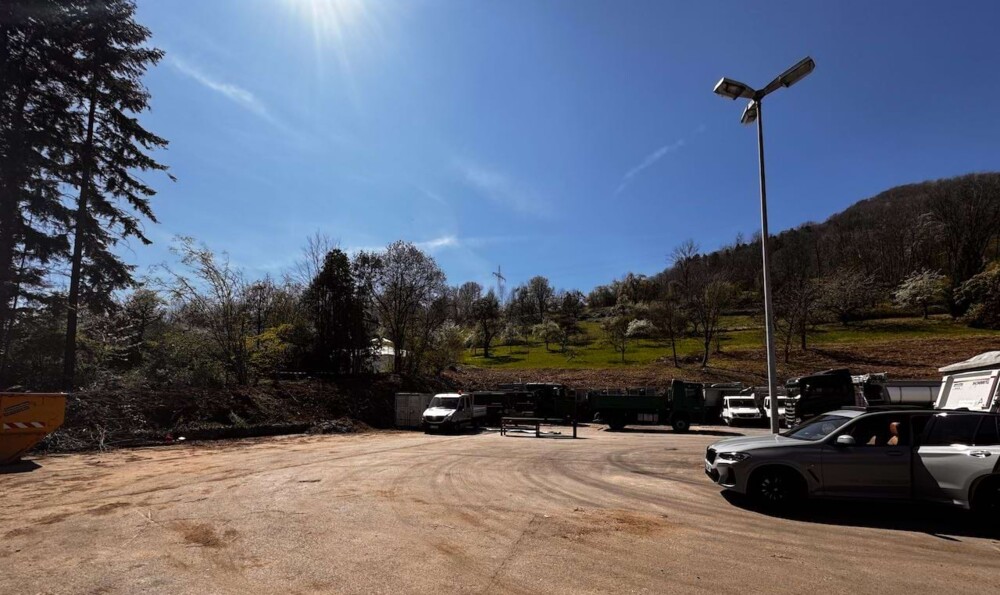 Baustelle mit unbefestigtem Boden, mehreren geparkten Fahrzeugen und Bäumen im Hintergrund unter klarem Himmel