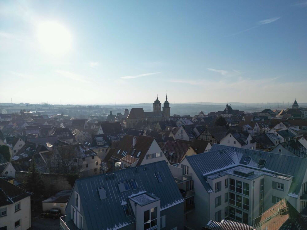 Dach eines Gebäudes mit leichtem Schneebelag, umgeben von Straßen und weiteren Häusern in einer Stadt