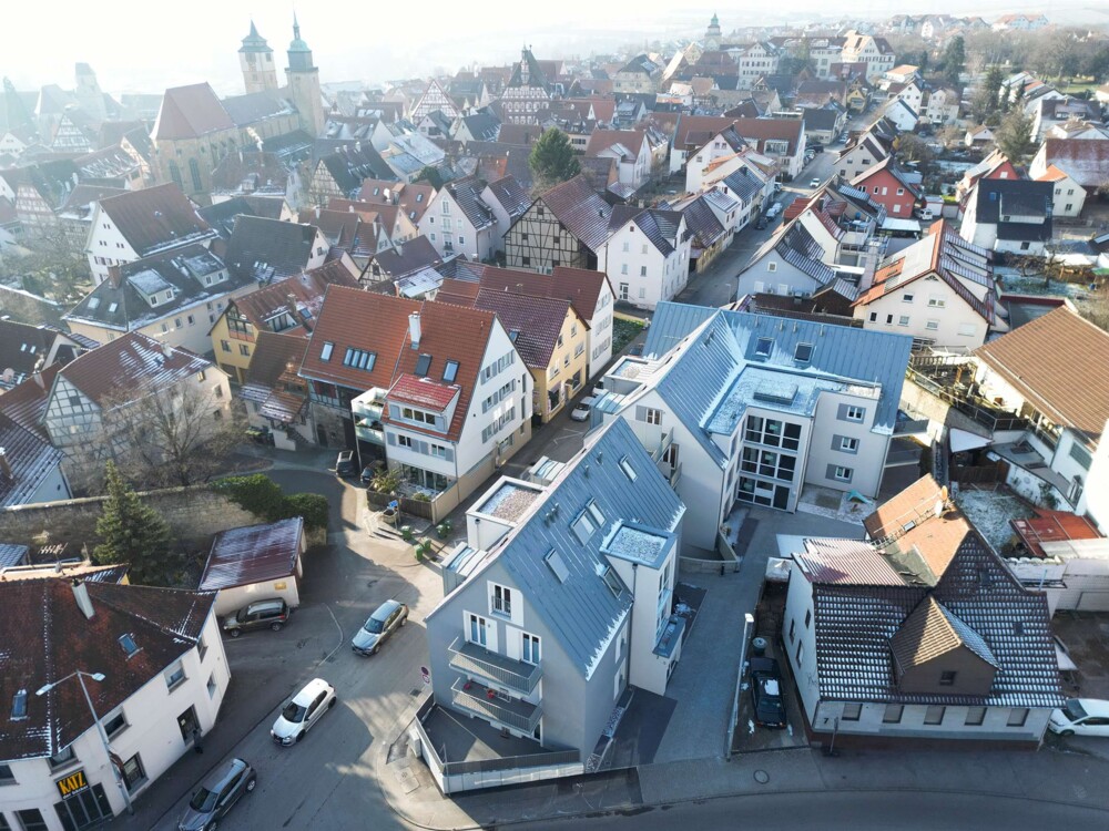Dach eines Gebäudes mit leichtem Schneebelag, umgeben von Straßen und weiteren Häusern in einer Stadt